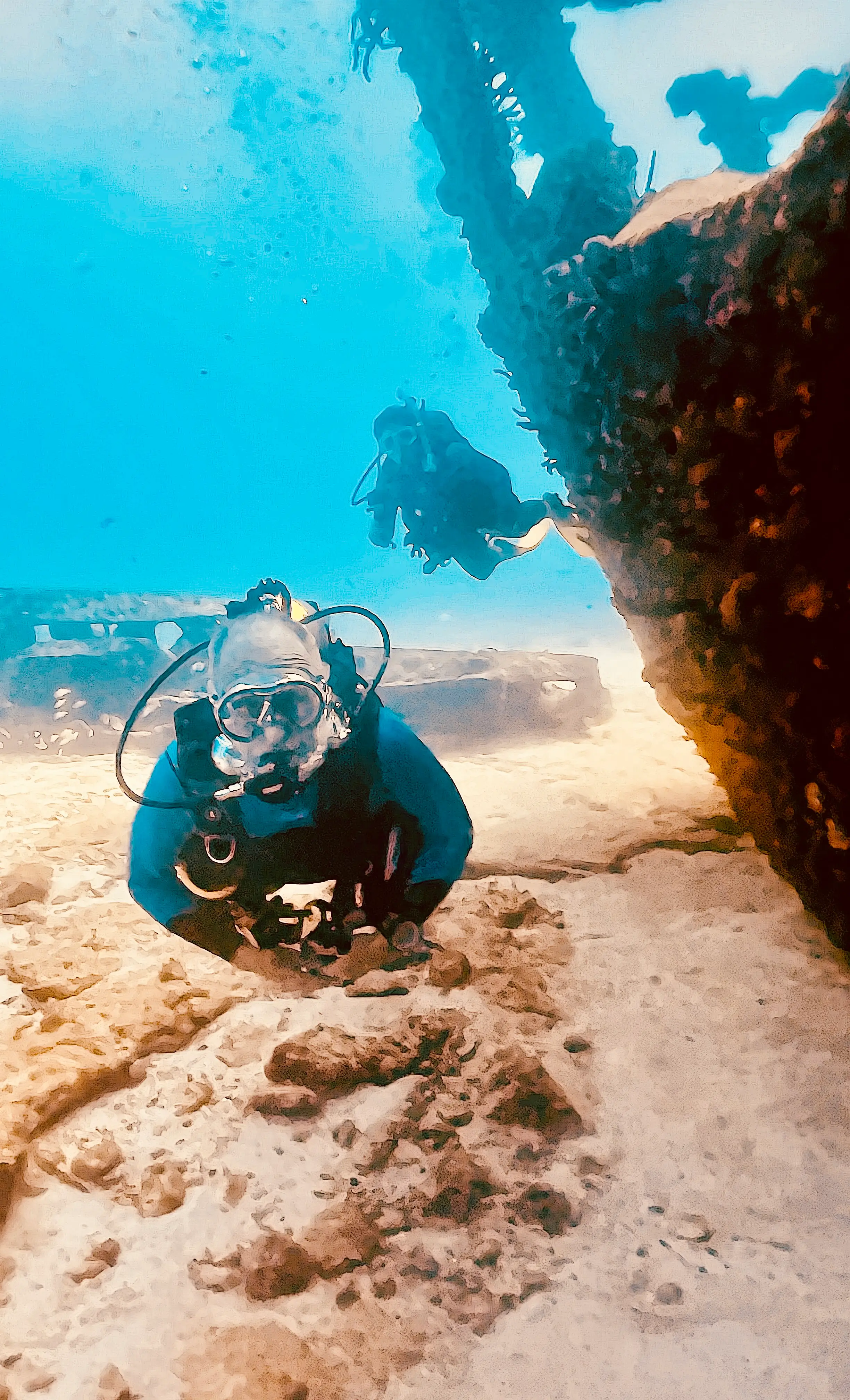 Two divers in detailed scuba gear explore a shipwreck with a rugged, corroded structure in a dynamic underwater setting.